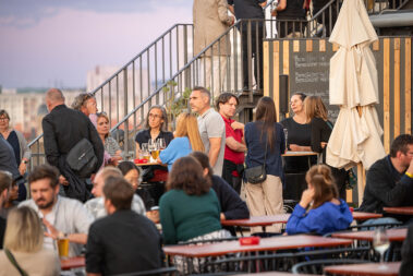 Personen unterhalten sich im Stehen oder im Sitzen an Tischen