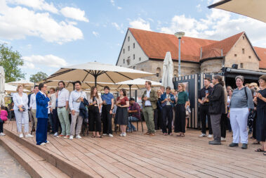 Präsidentin der AKT eröffnet das Sommerfest, mehrere Personen stehen und hören zu